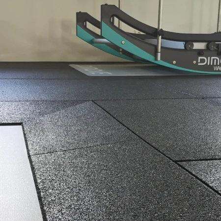 Das Bild zeigt einen modernen Fitnessbereich, der mit hochwertigen WARCO Fitnessbodenplatten ausgestattet ist. Der Bodenbelag besteht aus strapazierfähigem Gummi, das eine rutschfeste und stoßdämpfende Oberfläche bietet, ideal für intensive Trainingseinheiten. Der Boden ist in einem eleganten, mattschwarzen Finish gehalten, das sowohl funktional als auch ästhetisch ansprechend ist. Im Hintergrund des Bildes ist ein Trainingsgerät mit der Aufschrift "DIMOVE" zu sehen, das auf dem rutschfesten Bodenbelag sicher positioniert ist. Die klaren Linien der Bodenplatten und das minimalistische Design des Raumes unterstreichen die professionelle und hochwertige Ausführung des Fitnessbereichs, der sowohl für Einzel- als auch für Gruppentraining geeignet ist.