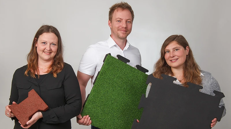 S prijaznim nasmehom trije svetovalci podjetja WARCO predstavljajo talne plošče iz z PU vezanega gumiranega granulata v rjavi, zeleni in črni barvi. Plošče so namenjene balkonom, saj zagotavljajo nedrsečo in trpežno površino. Vsaka različica ima edinstven dizajn in je enostavna za polaganje. Zahvaljujoč strokovnemu znanju svetovalcev boste izbrali primerno rešitev za varen in privlačen balkon. Plošče zahtevajo malo vzdrževanja in nudijo dodatno udobje.