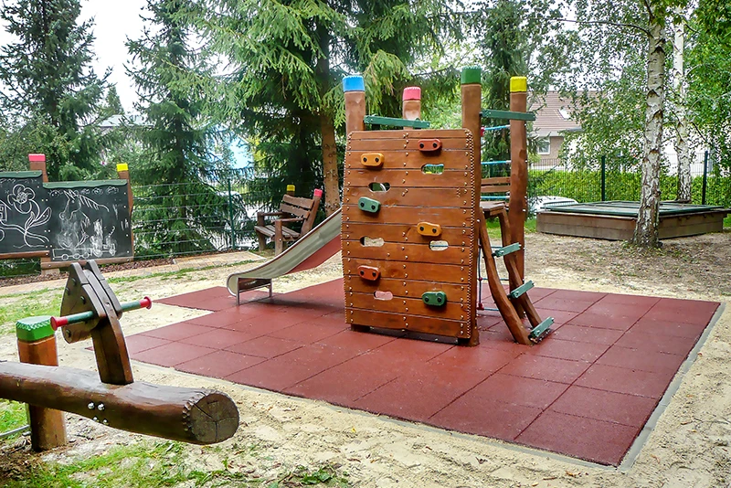 naturnaher Spielplatz mit Fallschutzplatten Fallschutz aus roten Fallschutzplatten rund um Kletterturm auf Spielplatz, wartungsfrei und stoßdämpfend.
