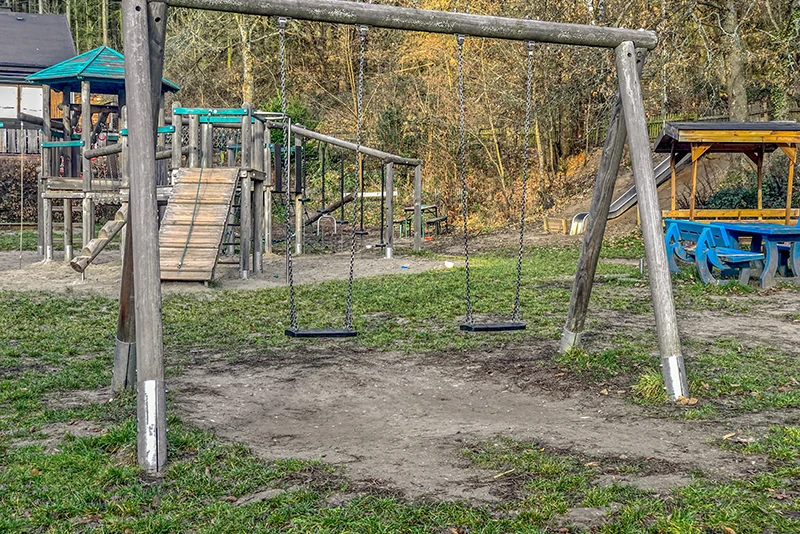 Doppelschaukel auf einem Spielplatz ohne Fallschutzmatten.