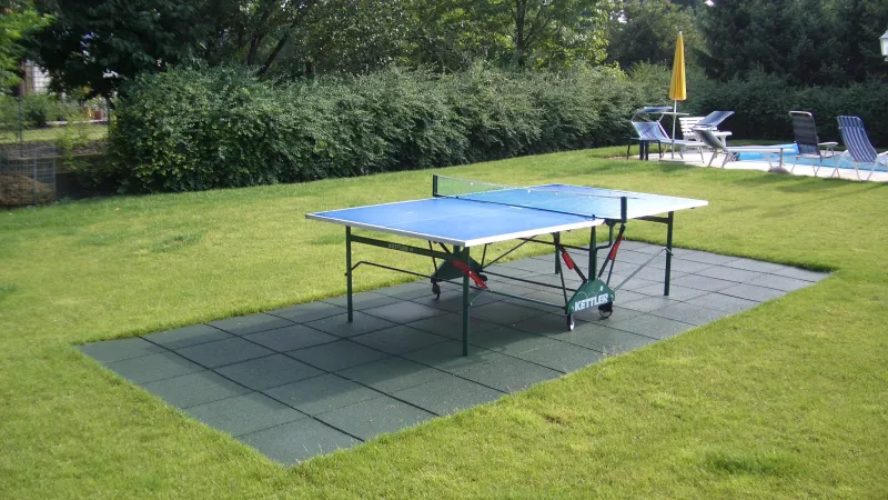 Under a table tennis table in the garden is a sports floor made of green WARCO safety tiles.
