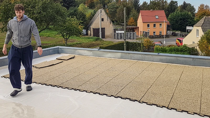 Na fotografiji oseba polaga bež WARCO puzzle plošče na prostoren balkon. Zaradi natančnega sestavljivega sistema je namestitev hitra in preprosta. Nedrseča in vremensko odporna površina ščiti podlago ter nudi pohodnost za različne namene. Tako nastane varen, udoben in preprosto vzdrževan zunanji prostor, idealen za sprostitev. Poleg tega izolacijski učinek pomaga zmanjšati hrup korakov.